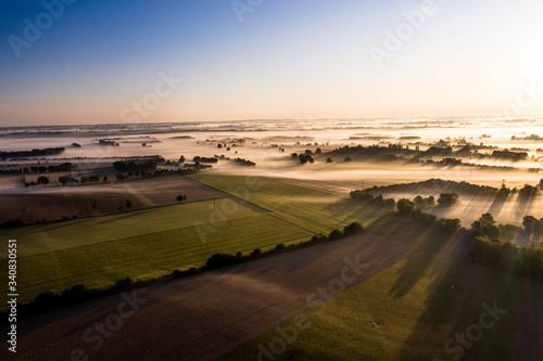 Aerial view of fields and trees under with fog