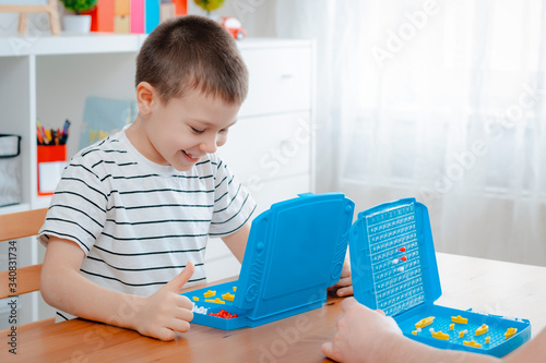 Boy child with dad playing warships and submarines are placed on the playing field in the game battleship. entertainment