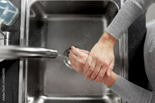 hygiene, health care and safety concept - close up of woman washing hands with liquid soap in kitchen at home