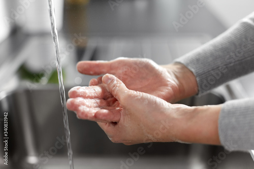 hygiene, health care and safety concept - close up of woman washing hands with soap and water in kitchen at home