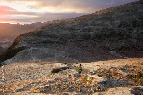 KESWICK, ENGLAND, UK - NOVEMBER 30, 2019: A fell runner descending rocky mountain trail from the summit of Cat Bells towards Maiden Moor at sunrise on a cold winters morning in the Lake District, UK Fototapeta