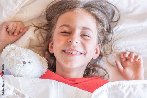 Portrait of a beautiful girl child pretending to be sleeping under the white blanket in the early morning.