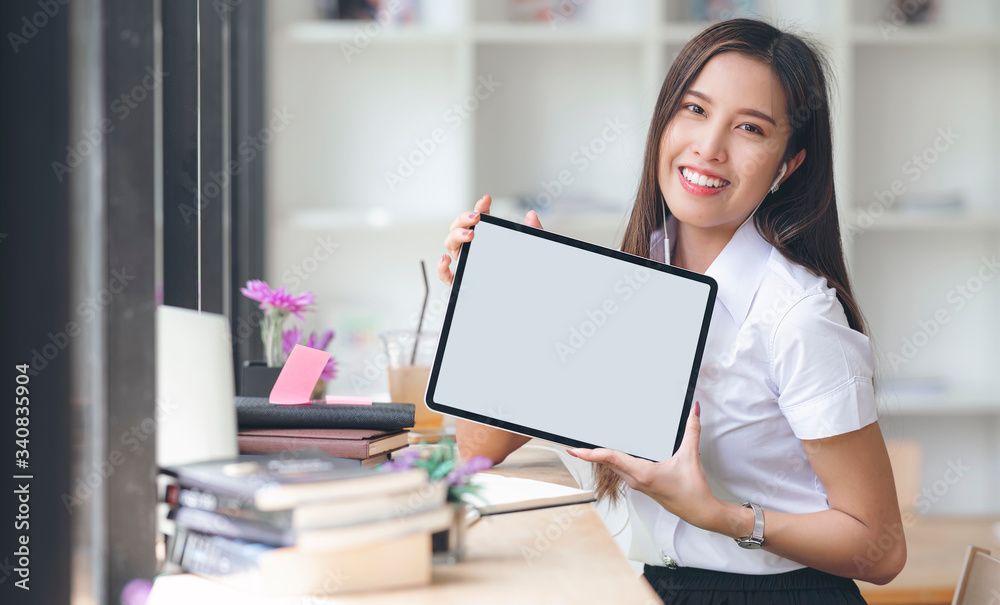 Young beautiful university student smiling and holding tablet with blank screen while sitting in co-workspace. Young beautiful university student smiling and holding tablet with blank screen while sitting in co-workspace.