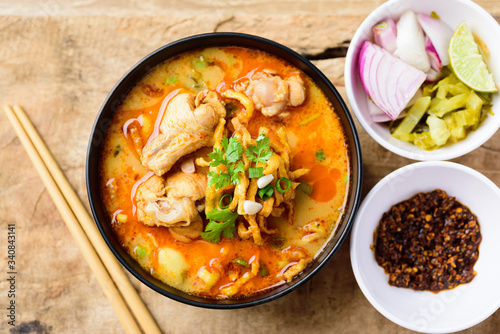Northern Thai food (Khao Soi), spicy curry noodles soup with coconut milk and chicken in a bowl on wooden background