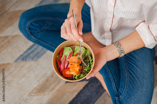 Girl holds a paper plate with healthy food sitting on the floor. Home delivery food. Healthy eating concept.