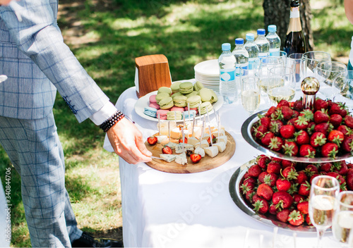 a man in a light blue suit takes food from a catering table with strawberries, cheese and glasses