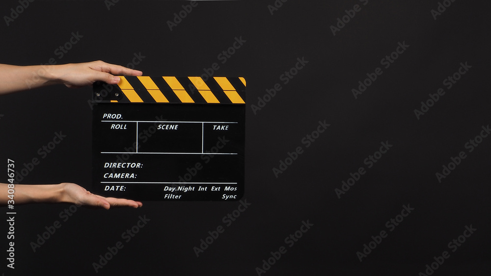 Hand is holding Black with yellow color clapper board or movie slate use in video production and movie industry on black background.