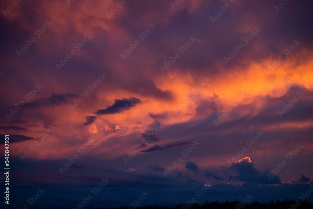 Bright red sunset among blue clouds. Mystical silhouettes in clouds