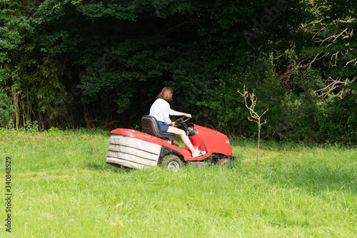 woman gardener with red modern tractor in field garden job driving a lawn mower