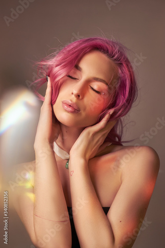 Art beauty portrait of a woman with pink hair, creative coloring. Bright colored highlights and shadows on the face, a girl with jewelry. Dyed hair in the wind