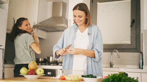 Two young beautiful women girlfriends lesbian couple cook at home in the kitchen cuddling and laughing merrily, home activism, cooking, recipes, staying at home.
