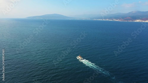 Aerial view of small ship sailing along sea bay, mountains on background
