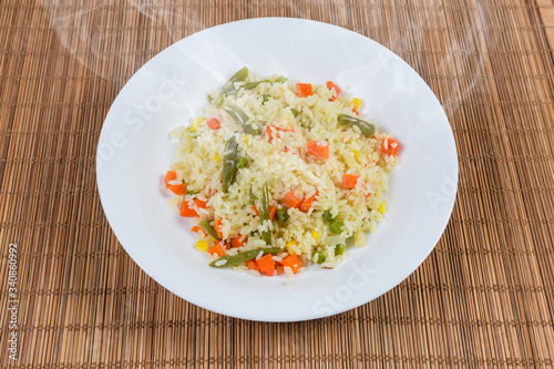 Rice boiled with vegetables on dish on bamboo table mat