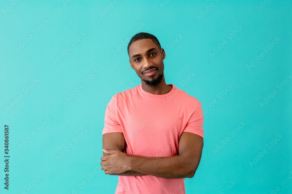 © Carlos David - Portrait of a young man smiling with arms crossed, against blue studio background