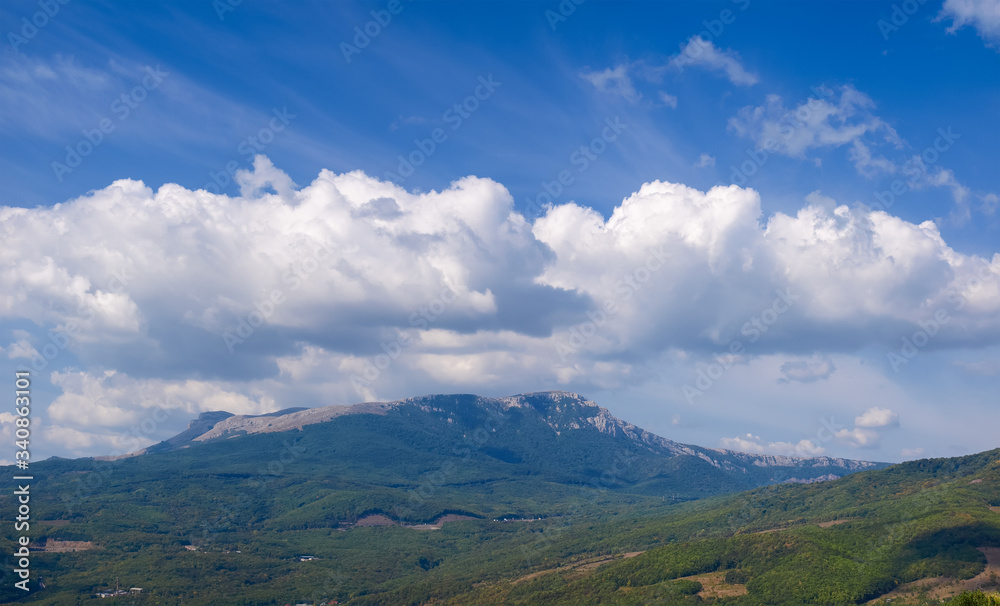 Sky with clouds over mountain with slopes covered with forests