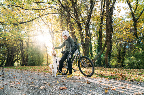 19/4/2020 Asian woman with a bike feeding a dog in autumn at the Botanic garden, Oamaru, New Zealand. Concept about exercise while social isolation from Coronavirus or Covid 19.