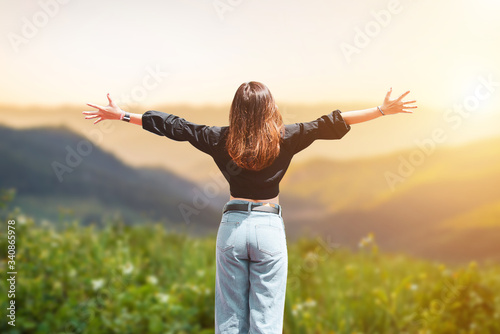 Freedom and enjoy with nature. Young woman relaxing and looking beautiful view in summer sunrise sky outdoor in holiday at National Park. She raised both hands above the head, showing joy and success.