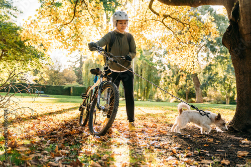 19/4/2020 Asian woman with a bike walking with a dog in autumn at the Botanic garden, Oamaru, New Zealand. Concept about exercise while social isolation from Coronavirus or Covid 19.