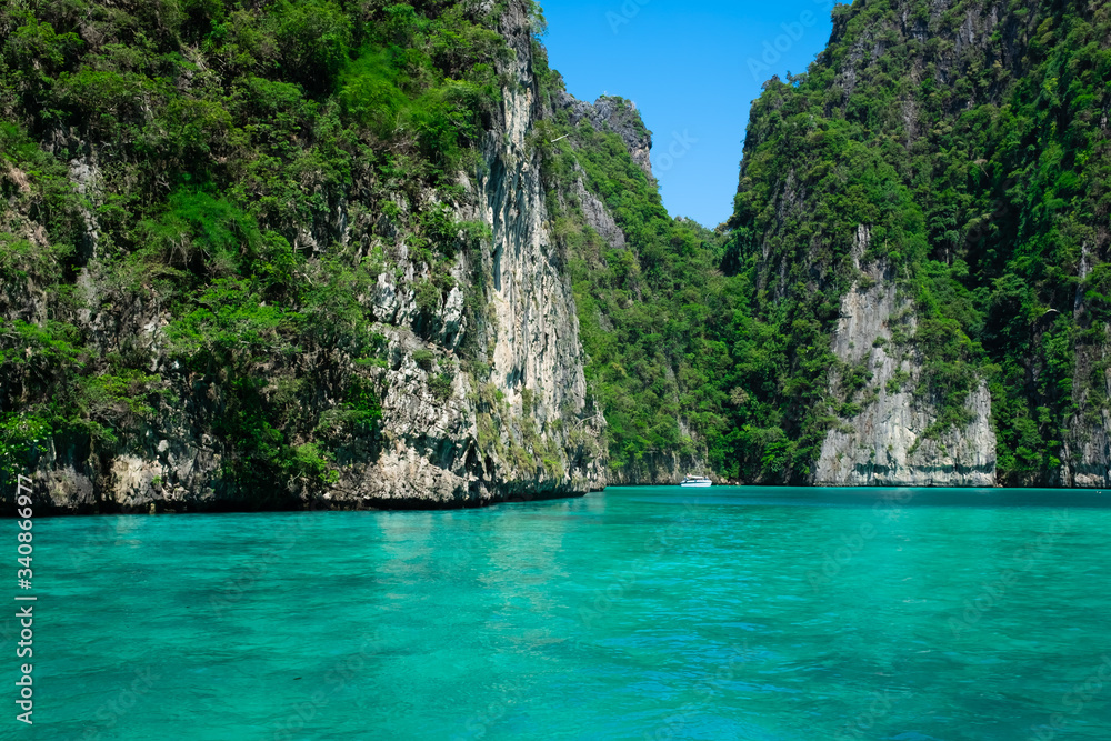 Fototapeta premium Beautiful turquoise green Pileh Lagoon water with a small white boat in the middle surrounded by steep limestone hills at Phi Phi Island archipelago, Krabi province, Thailand.