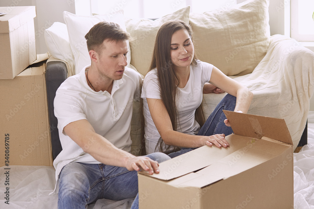 Portrait of happy couple looking at laptop computer together sitting in new house, surrounded with boxes