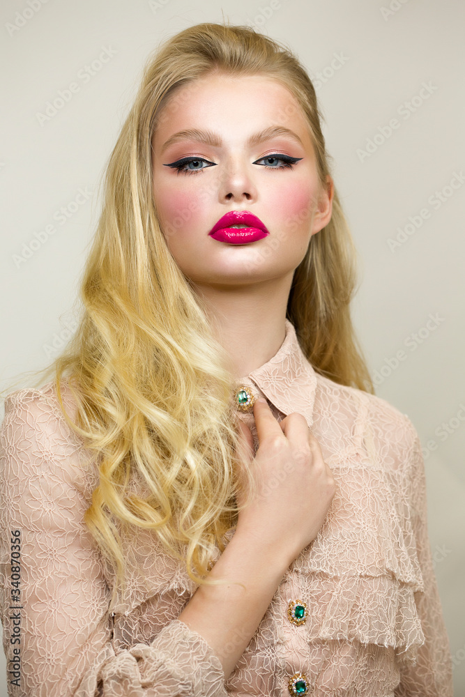 Portrait of a young woman in a pink dress. Bright makeup, pink lipstick and  black arrows on the eyes. She is looking straight. The hand moves the  collar and button. Stock Photo