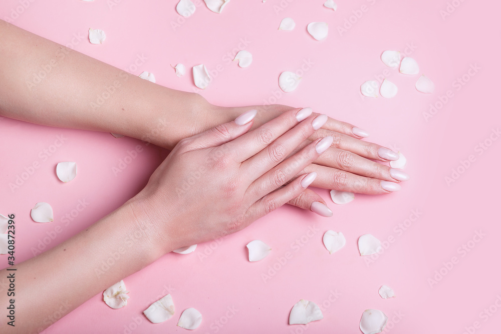 Female's hands rubbing cosmetic cream into skin on on pink background with roses petals, top view. Female's hands rubbing cosmetic cream into skin on on pink background with roses petals, top view.