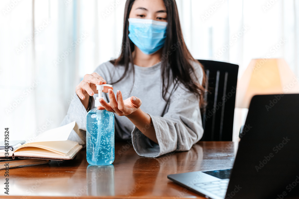 Working from home. Cleaning hands with sanitizer gel. Business woman working from home wearing protective mask.