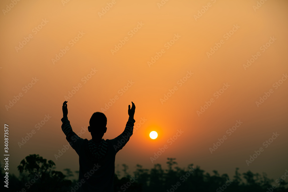 Boy lift hands up and praying to God on sky with light sunset background, Christians should worship and thank God, christian silhouette concept.