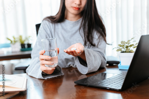 Businesswomen working at home with glass of water takes white round pill in hand.