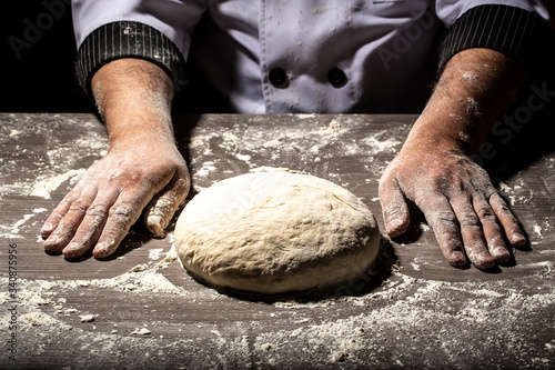 Beautiful and strong men's hands knead the dough from which they will then make bread, pasta or pizza. A cloud of flour flies around like dust. Food concept