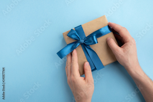 Gift box in a man hands on light blue background. Fathers day, birthday and holiday concept. Top view, flat lay, copy space