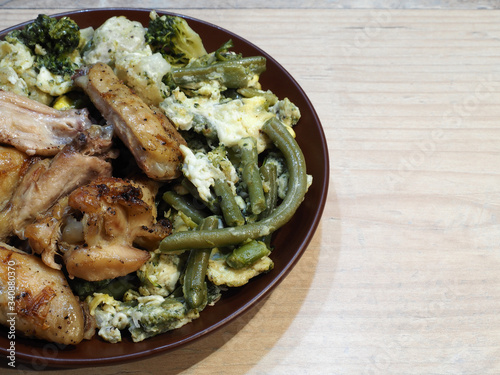 Grilled chicken wings, green string beans, cauliflower and broccoli with fried egg in a brown plate on a light wooden background. Traditional meat dish with vegetables for lunch closeup, top view