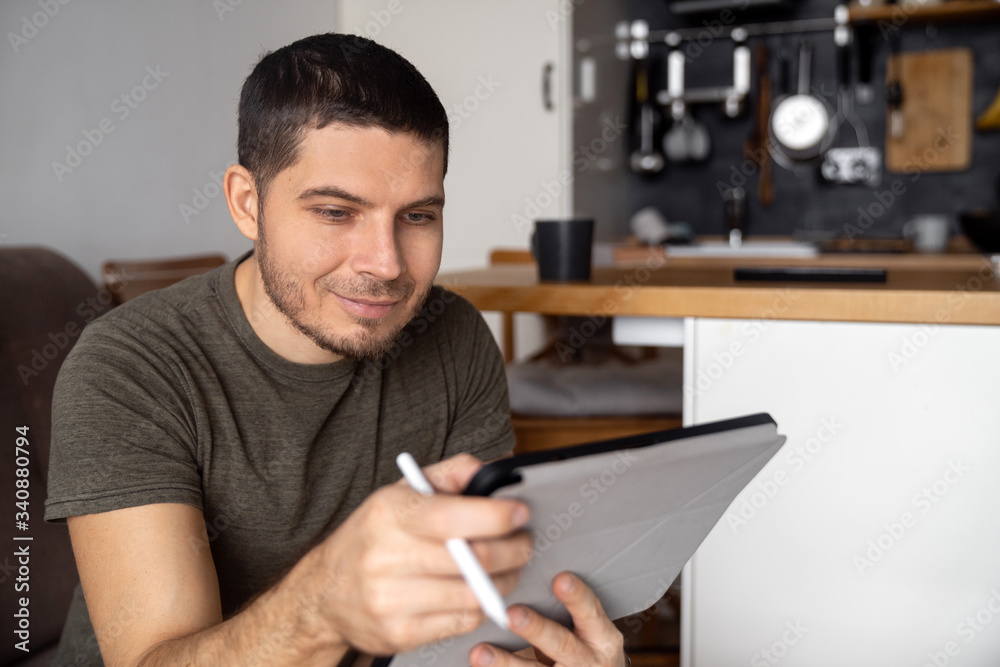 A man at home sitting on the couch uses a tablet and pen to search the Internet for news on a business note. Remote home work. Quarantine A man at home sitting on the couch uses a tablet and pen to search the Internet for news on a business note. Remote home work. Quarantine
