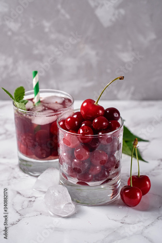 Fresh cherry lemonade with ice  mint and paper straw in sparkling glasses on table  copy space. Cold summer drink. Berry cocktail