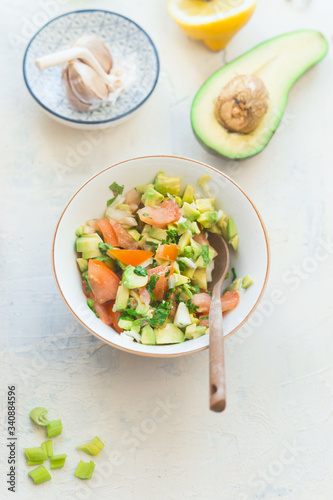 Tasty fresh avocado tomato salsa salad on white kitchen table background, top view. Healthy food.  Vegetarian lunch or snack