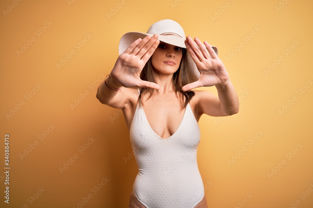 Young beautiful brunette woman on vacation wearing swimsuit and summer hat doing frame using hands palms and fingers, camera perspective Young beautiful brunette woman on vacation wearing swimsuit and summer hat doing frame using hands palms and fingers, camera perspective