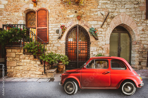 Old vintage italian scene. Small antique red car. Fiat 500. Old Italian house with outside a small subcompact old nostalgia red car, fiat 500. Vintage scene. Assisi, Italy. photo