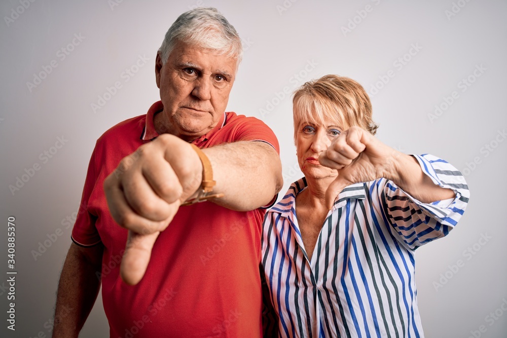 Senior beautiful couple standing together over isolated white background looking unhappy and angry showing rejection and negative with thumbs down gesture. Bad expression. Senior beautiful couple standing together over isolated white background looking unhappy and angry showing rejection and negative with thumbs down gesture. Bad expression.