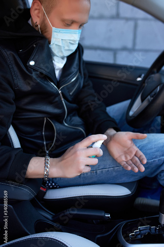 Man in protection mask sitting in the car, spraying hands antibacterial sanitizer spray for prevention coronavirus