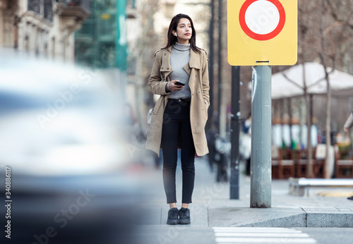 Vászonkép Pretty young woman crossing the street while listen to music with the wireless earphones
