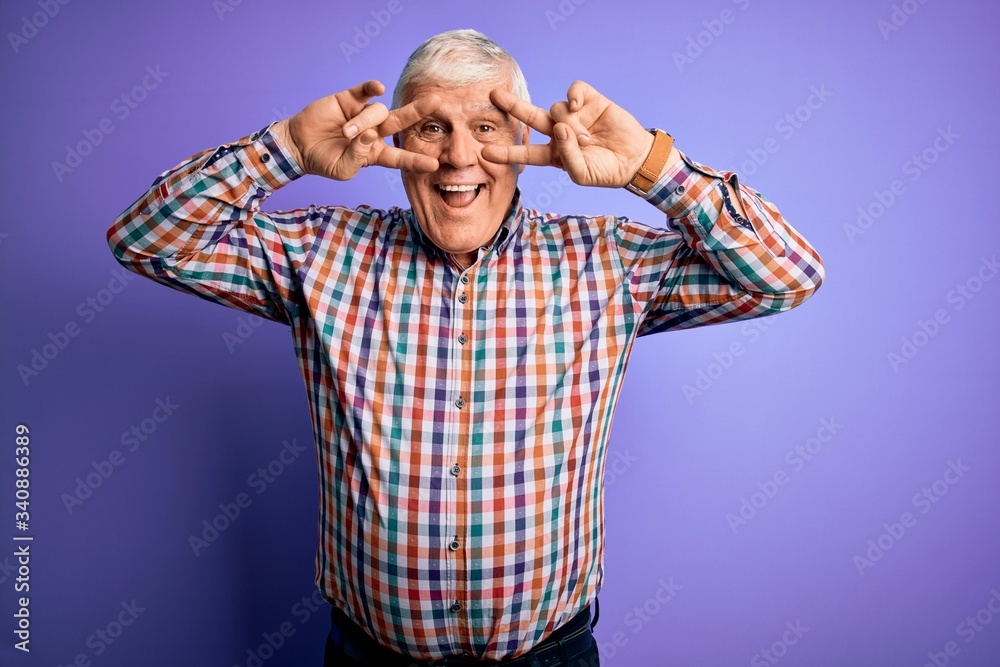 Senior handsome hoary man wearing casual colorful shirt over isolated purple background Doing peace symbol with fingers over face, smiling cheerful showing victory
