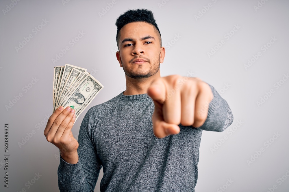 Young handsome man holding bunch of dollars banknotes over isolated white background pointing with finger to the camera and to you, hand sign, positive and confident gesture from the front Young handsome man holding bunch of dollars banknotes over isolated white background pointing with finger to the camera and to you, hand sign, positive and confident gesture from the front