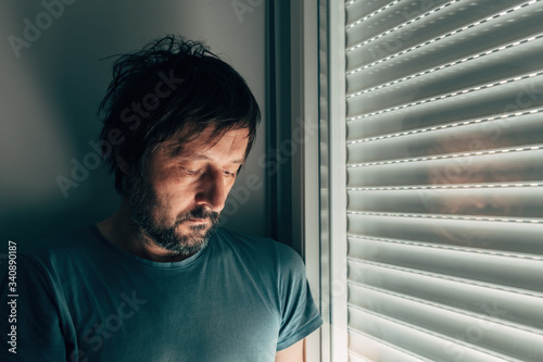 Sulking man by the window with shutters rolled down photo