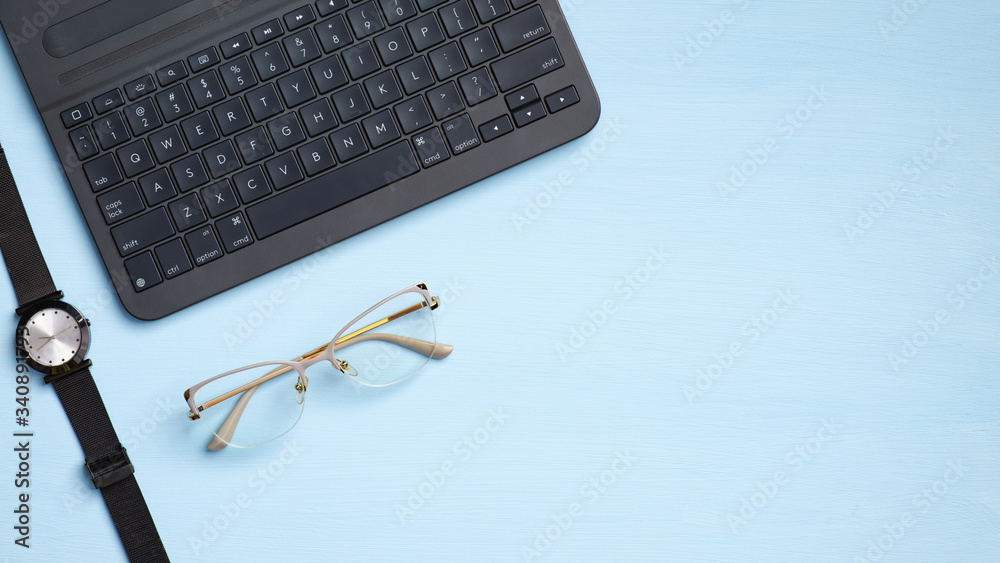 Fototapeta premium Stylish feminine workspace with laptop computer keyboard, watches, glasses on blue background. Modern home office desk, freelancer workplace. Flat lay, top view, copy space