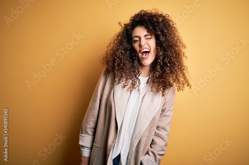 Young beautiful brunette woman with curly hair and piercing wearing casual t-shirt and diadem winking looking at the camera with sexy expression  cheerful and happy face.