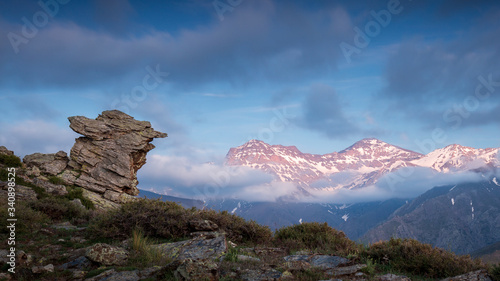 Panoramic view of the peaks of Sierra Nevada, Granada, Andalusia, at sunset between clouds. Rocky landmark in the foreground and snowy mountains in the background. photo