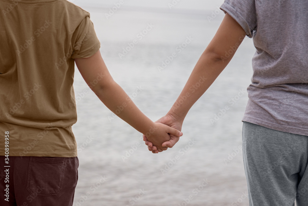 Two children hold hands in front of the sea on the beach, during a cloudy day. Concept of company facing the unknown. Two children hold hands in front of the sea on the beach, during a cloudy day. Concept of company facing the unknown.