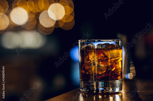 glass with whiskey and ice cubes on the bar with bokeh on background