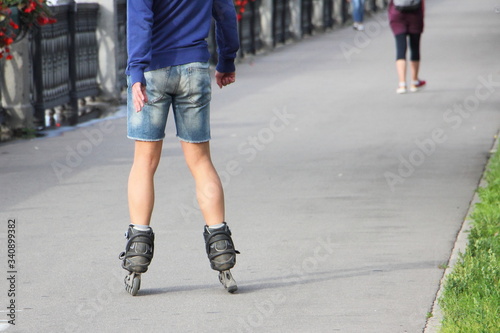 A man in shorts without safety equipment skating with rollerblades on a asphalt road alley in Park at summer day, waist-high rear view close up, city vacation activity outdoors 