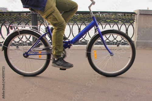 One cyclist man in casual clothing rides on a utility folding bicycle close up on asphalted road quayside on a summer day, waist-high side view. Ecological transport